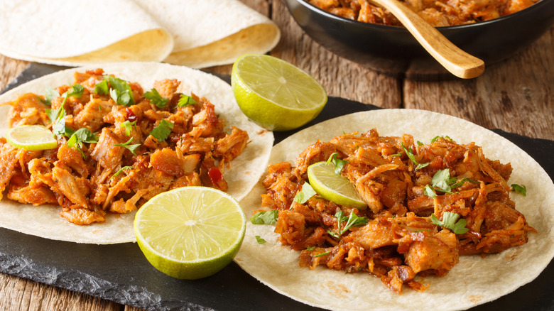 two tortillas with chilorio and lime wedges on black plate