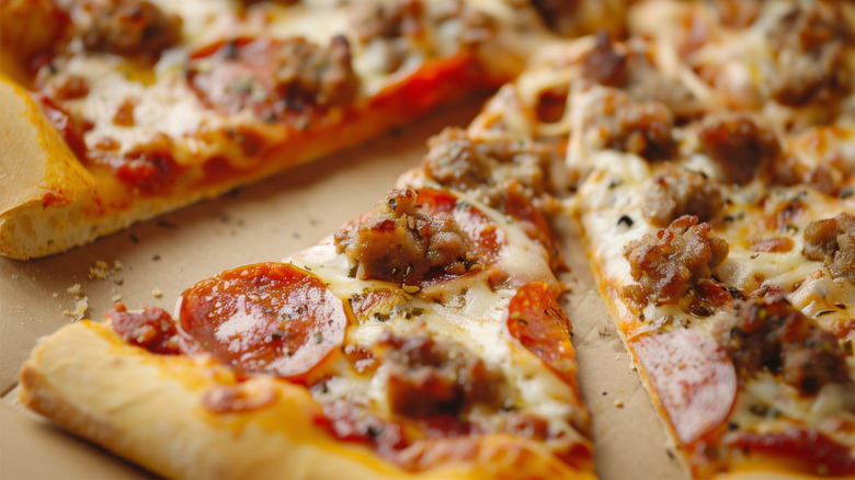 close-up shot of a pepperoni and sausage pizza in a takeout box